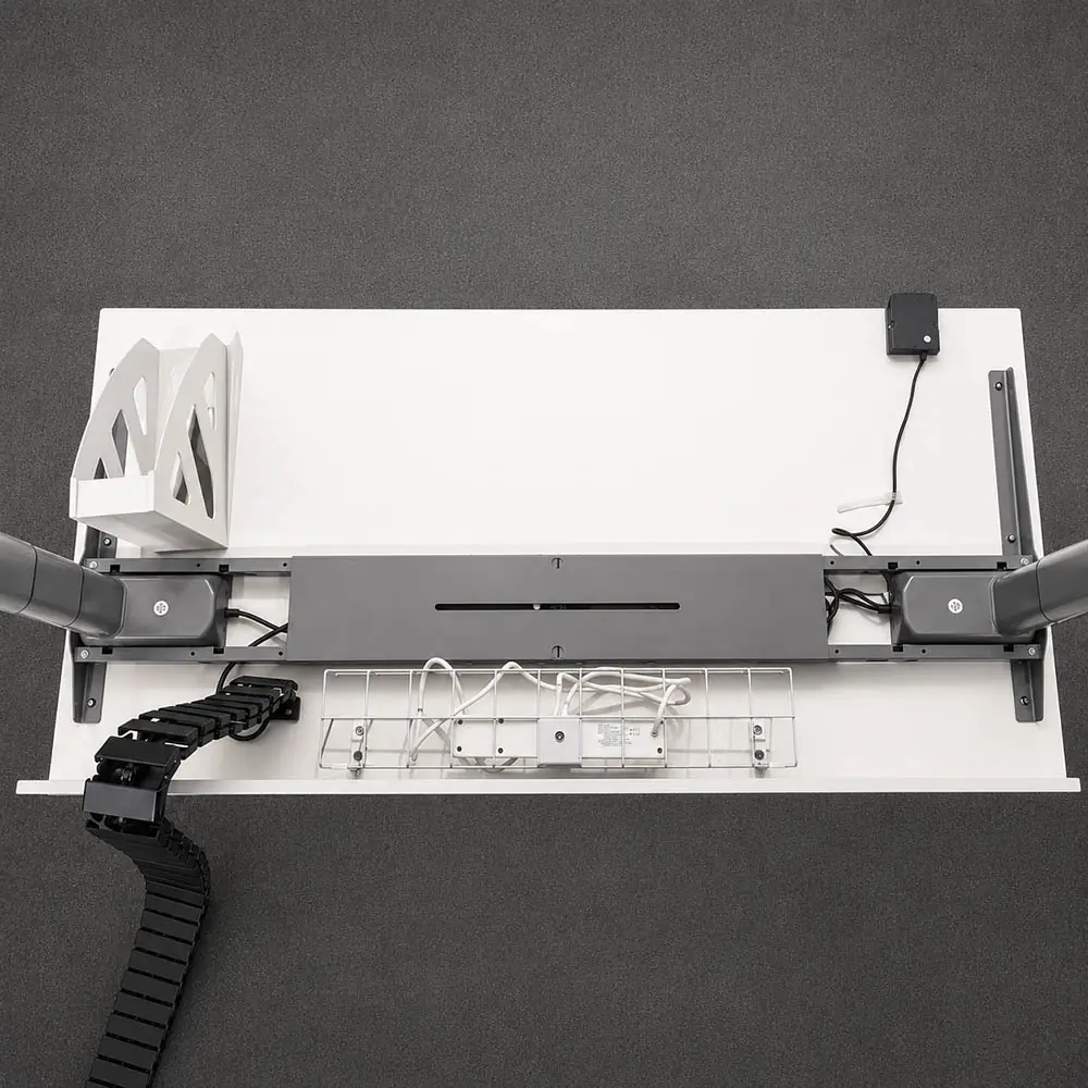 underside view of a standing desk showing frame structure, control box, cable routing, and under-desk accessories