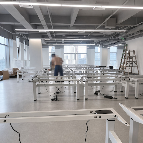 rows of white standing desk frames with control cables during office workstation assembly