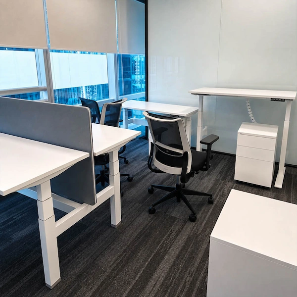 several white height adjustable desks at different heights with chairs divider screens and storage units visible around the desk travel area